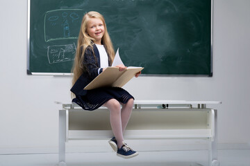 Beautiful little schoolgirl sitting on desk. Photo session in the studio - obrazy, fototapety, plakaty