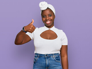 Young african woman with turban wearing hair turban over isolated background doing happy thumbs up gesture with hand. approving expression looking at the camera showing success.