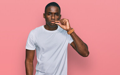 Young african american man wearing casual white t shirt mouth and lips shut as zip with fingers. secret and silent, taboo talking © Krakenimages.com