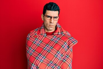 Handsome hispanic man wrapped in a red warm red blanket skeptic and nervous, frowning upset because of problem. negative person.
