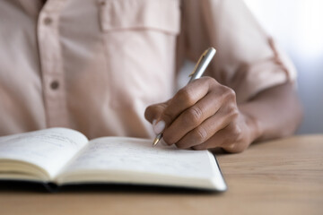 Crop close up of African American woman write take notes in notebook, engaged in time management at...