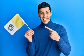 Handsome hispanic man holding vatican city flag smiling happy pointing with hand and finger