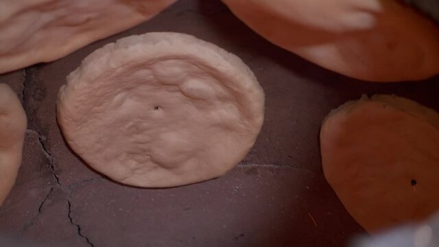 There are preparing process of pitta bread in tandoori. Traditional oriental flat bread. Baker is attaching the dough on tandoori wall, close-up 