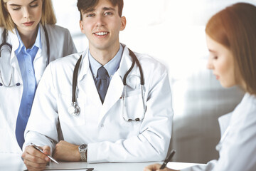 Fototapeta premium Group of young doctors are discussing disease treatment in modern hospital office. Coronavirus countering, patient help in medicine concept