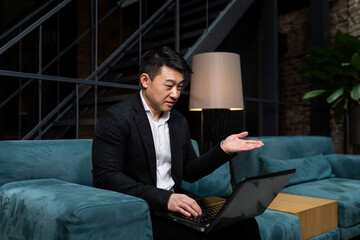 Successful Asian businessman, in a black business suit, works on a laptop, relaxes in a restaurant or hotel, and in a stylish office explains a new business strategy via video link