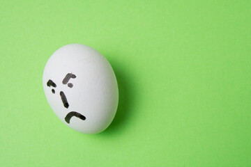 An egg with an evil face, on a green background with copy space.