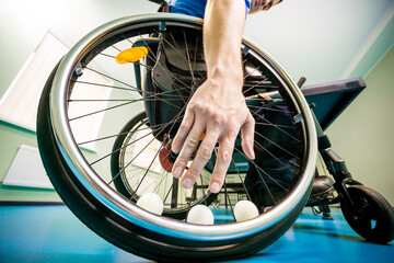 Fototapeta na wymiar Disabled man in a wheelchair play at table tennis. Hand takes a ball fixed in a wheel