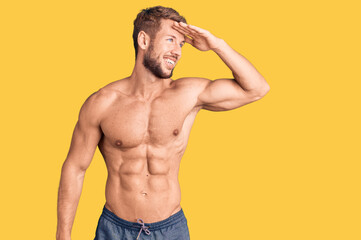 Fototapeta premium Young caucasian man standing shirtless very happy and smiling looking far away with hand over head. searching concept.