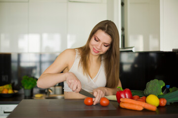 young sportive woman stands in the kitchen, preparing a healthy meal, a mix of vegetables