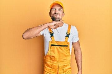 Young handsome man wearing handyman uniform over yellow background cutting throat with hand as knife, threaten aggression with furious violence