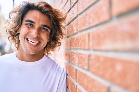 Young handsome hispanic man smiling happy leaning on the wall at street of city