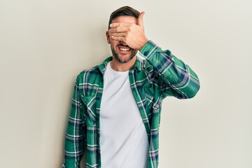Handsome man with beard wearing casual clothes smiling and laughing with hand on face covering eyes for surprise. blind concept.