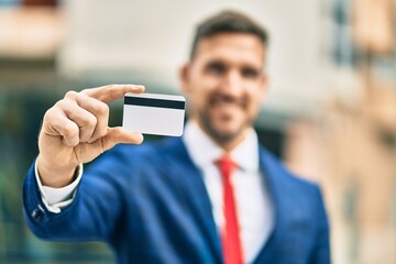 Young caucasian businessman smiling happy holding credit card at the city.