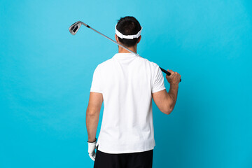 Young handsome man isolated on blue background playing golf and in back position