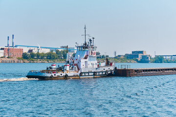 towboat pushes dry bulk cargo barge on the river in an industrial landscape