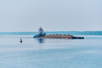 pusher tug pushes dry bulk cargo barge with sand on the river in the morning haze