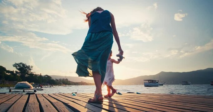 Family dances on pier. Woman and toddler girl dance and spin on the wooden pier during sunset