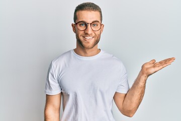 Young caucasian man wearing casual clothes and glasses smiling cheerful presenting and pointing with palm of hand looking at the camera.