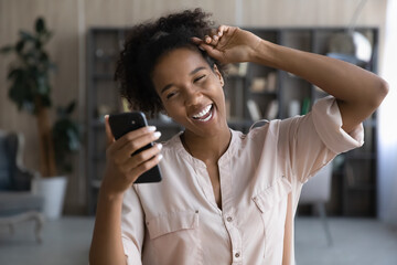 Overjoyed millennial African American woman modern cellphone laugh talk speak on video call online. Happy smiling young biracial female have fun using smartphone. Communication, technology concept.