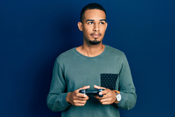 Young african american man playing video game holding controller smiling looking to the side and staring away thinking.