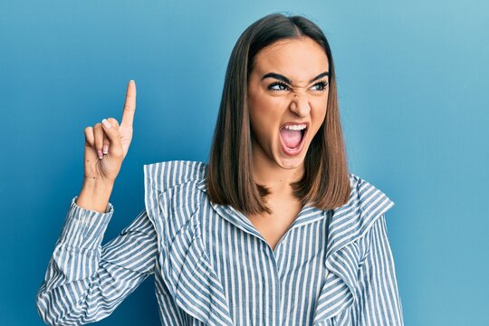 Young brunette student girl pointing up with finger angry and mad screaming frustrated and furious, shouting with anger. rage and aggressive concept.