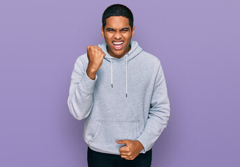 Young handsome hispanic man wearing casual sweatshirt angry and mad raising fist frustrated and...