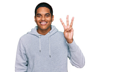 Young handsome hispanic man wearing casual sweatshirt showing and pointing up with fingers number three while smiling confident and happy.