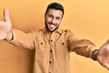 Young hispanic man wearing casual clothes looking at the camera smiling with open arms for hug. cheerful expression embracing happiness.