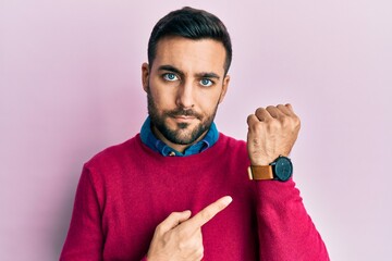 Young hispanic man wearing casual clothes in hurry pointing to watch time, impatience, looking at...