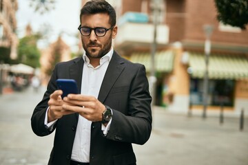 Young hispanic businessman with serious expression using smartphone at the city. - Powered by Adobe