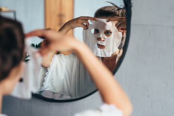 Woman applies a sheet mask to her face