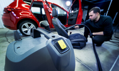 Naklejka premium Car service worker cleaning car seat with vacuum cleaner.