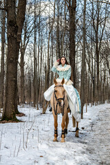 Fototapeta premium beautiful girl in a blue outfit and a light brown horse in a spring forest
