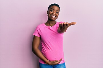 Young african american woman expecting a baby, touching pregnant belly smiling friendly offering handshake as greeting and welcoming. successful business.