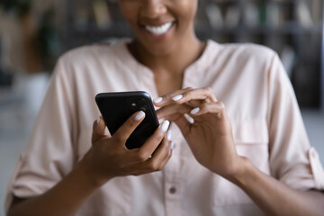 Crop close up of smiling biracial woman hold use modern cellphone text message online on gadget. Happy African American female browse internet or have webcam video talk on smartphone device.