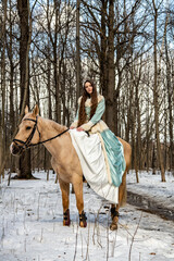 beautiful girl in a blue outfit and a light brown horse in a spring forest