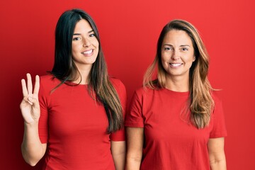 Hispanic family of mother and daughter wearing casual clothes over red background showing and pointing up with fingers number three while smiling confident and happy.
