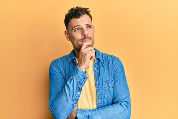 Young hispanic man wearing casual clothes thinking concentrated about doubt with finger on chin and...