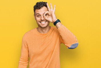 Young hispanic man wearing casual clothes doing ok gesture with hand smiling, eye looking through...