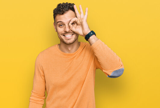 Young hispanic man wearing casual clothes doing ok gesture with hand smiling, eye looking through fingers with happy face.