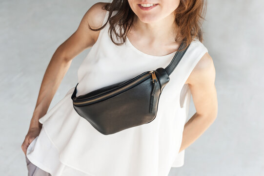 Leather Zipper Belt Pouch, Sling Crossbody Bag Women. Smiling girl in a white blouse on a light gray background carries a black leather banana bag.