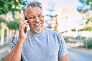 Middle age hispanic grey-haired man smiling happy talking on the smartphone at the city.