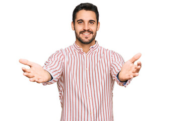 Fototapeta premium Young hispanic man wearing business shirt looking at the camera smiling with open arms for hug. cheerful expression embracing happiness.