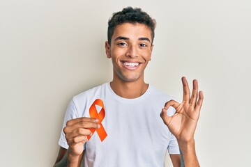 Young handsome african american man holding awareness orange ribbon doing ok sign with fingers,...
