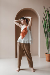 Caucasian young woman in a wide white blouse, brown trousers and an orange fringe bag.