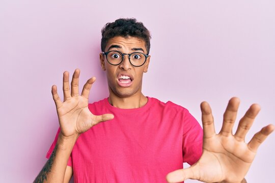 Young handsome african american man wearing glasses over pink background afraid and terrified with fear expression stop gesture with hands, shouting in shock. panic concept.