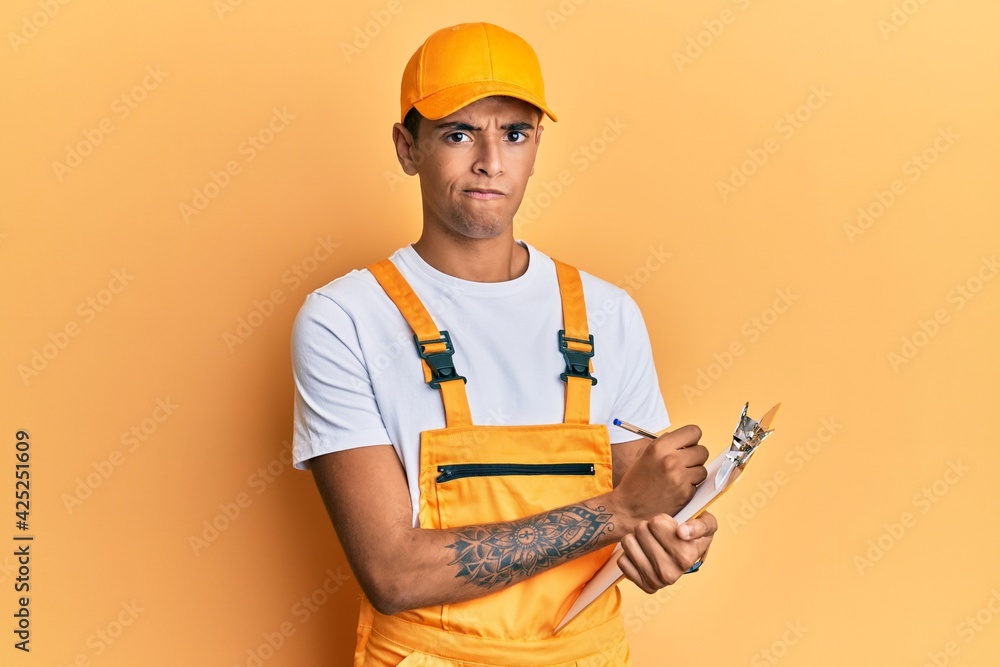 Sticker young handsome african american man wearing courier uniform holding clipboard skeptic and nervous, f