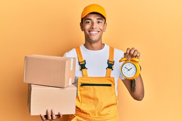 Young handsome african american man holding delivery box and alarm clock for express service smiling with a happy and cool smile on face. showing teeth.