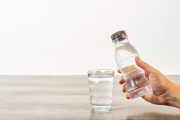 Female hand holding water bottle and glass on wooden table.