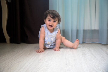 Baby Girl In Summer Dress Sit on wooden floor inside room.